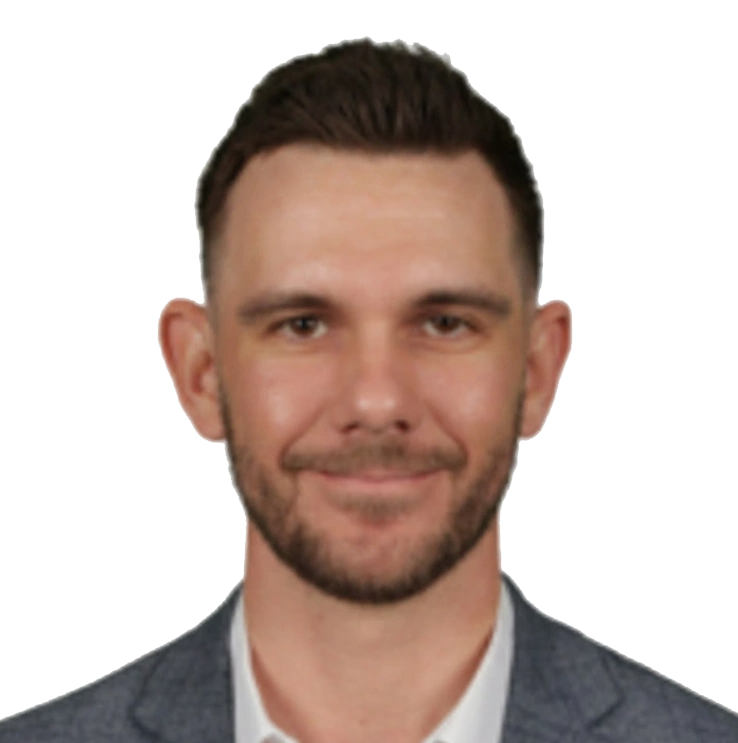 Head-and-shoulders portrait of a smiling man with short dark hair and a light beard, wearing a gray blazer and white shirt.
